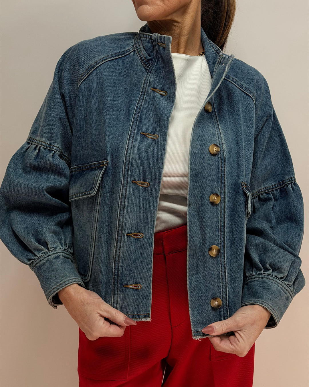 Person wearing a blue denim jacket over a white shirt and red pants on a beige background