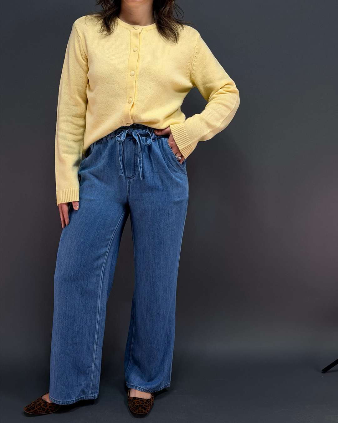 woman wearing a yellow cardigan with blue wide leg tie waist pants in front of a gray background