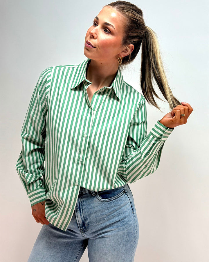 Woman wearing a green and white striped shirt and blue jeans against a plain background