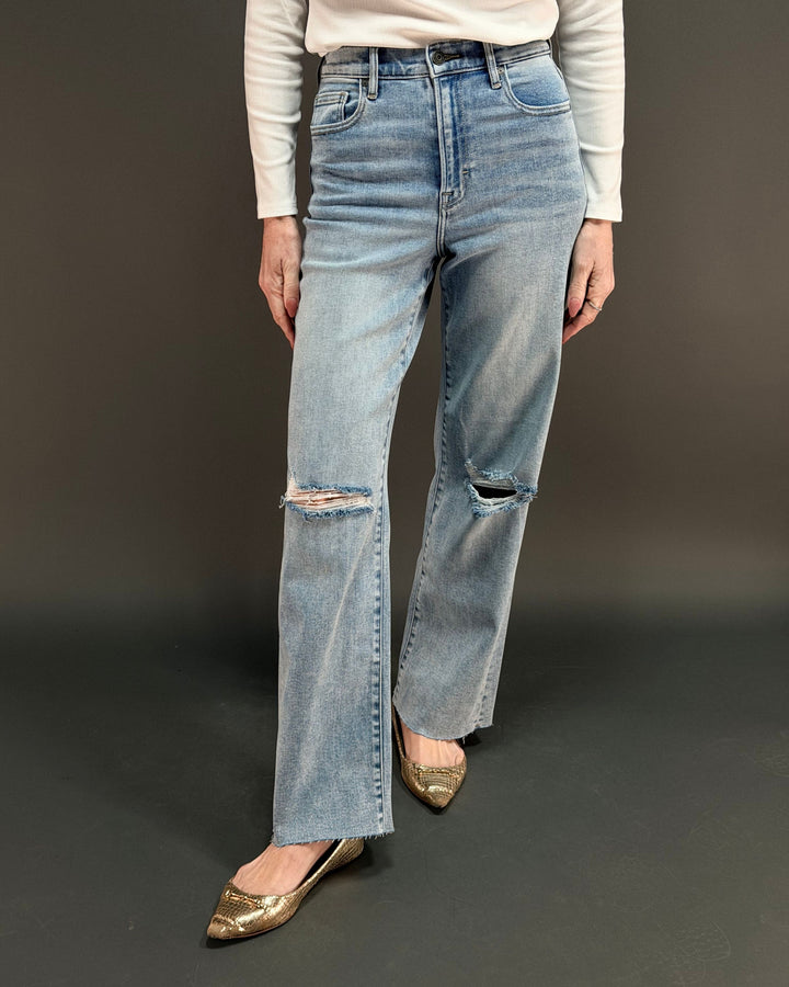 woman wearing light wash ripped jeans in front of gray background