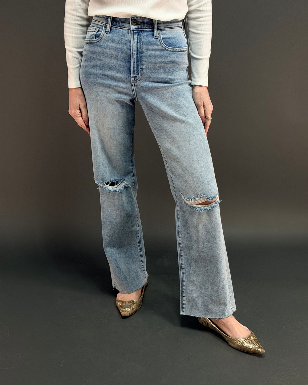 woman wearing light wash ripped jeans in front of gray background