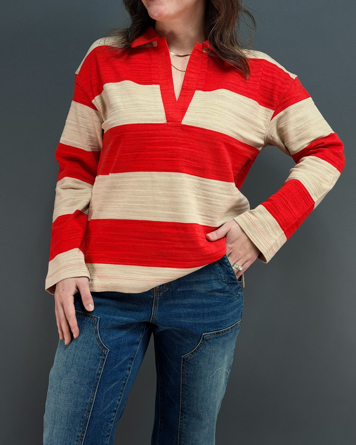woman wearing red and tan striped rugby top with jeans in front of a gray background