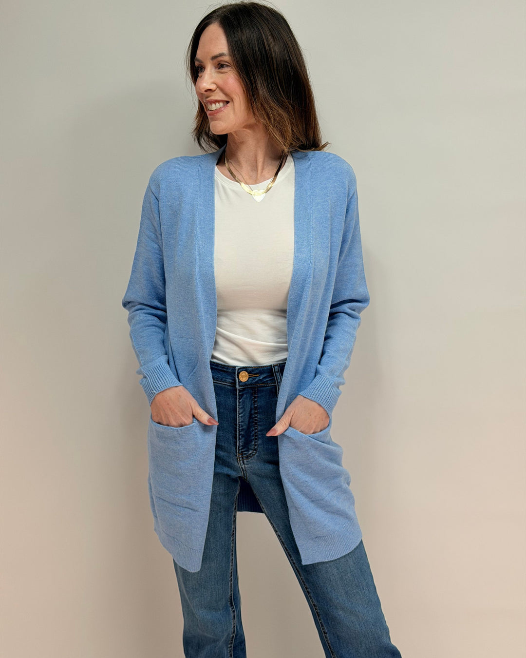 Woman wearing a light blue cardigan over a white shirt and jeans on a plain background
