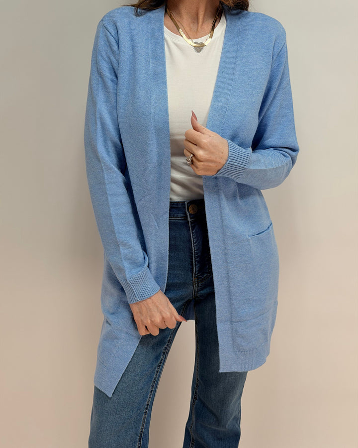 Person wearing a light blue cardigan over a white shirt and jeans on a beige background