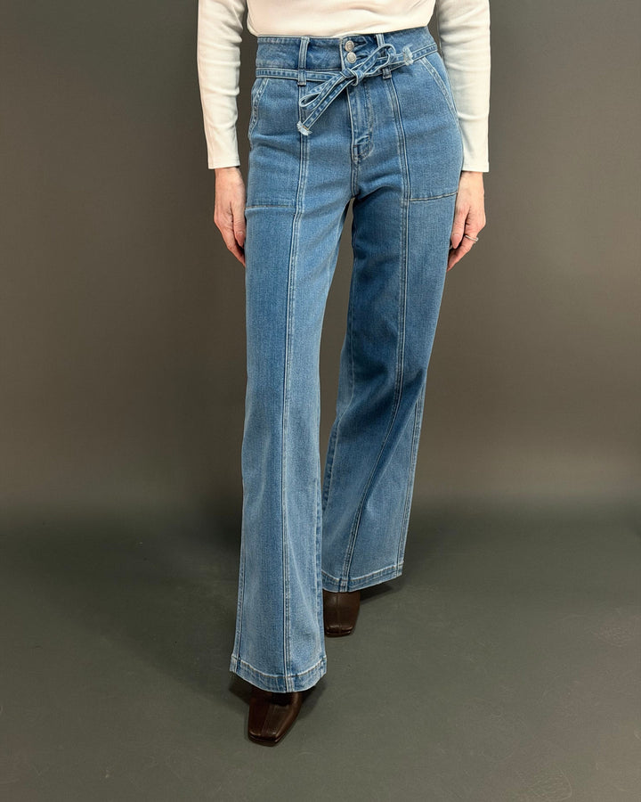 woman wearing tie waist wide leg jeans with a white shirt in front of gray background