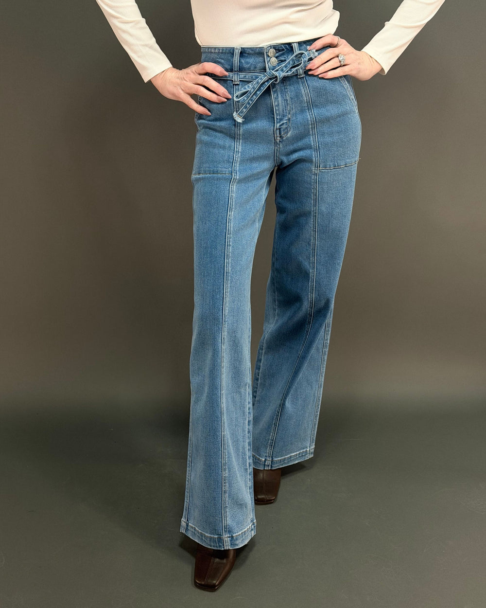 woman wearing tie waist wide leg jeans with a white shirt in front of gray background